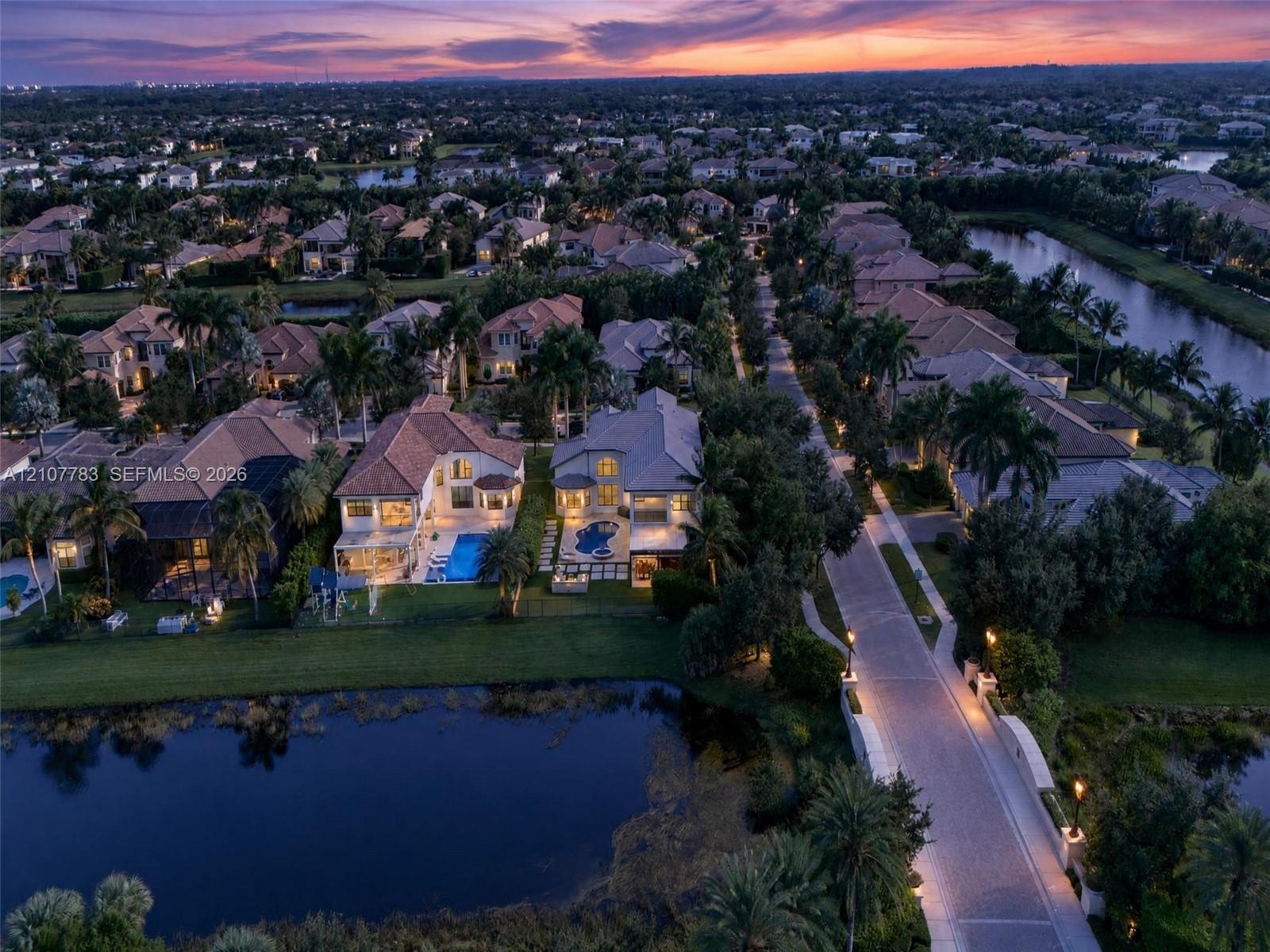 Aerial perspective of a residential neighborhood featuring waterfront lots, paved roadways, mature palm trees, and rear-yard swimming pools
