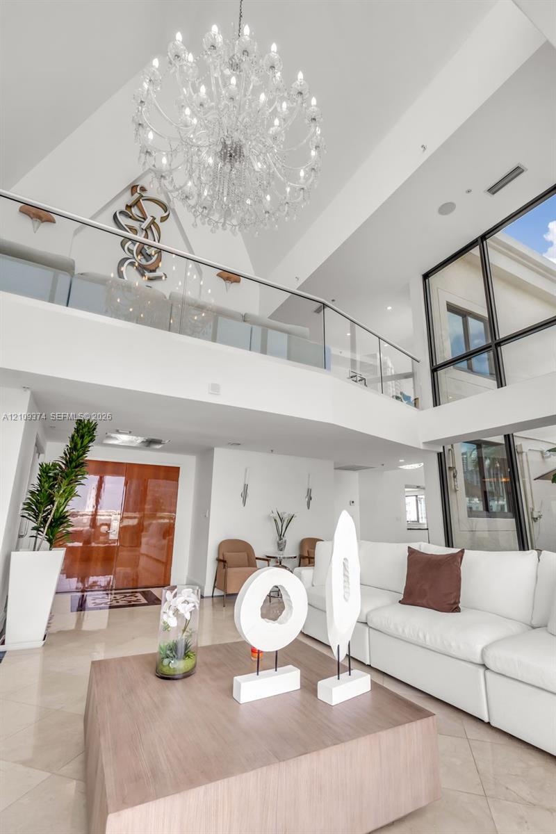 Two-story foyer featuring vaulted ceilings, floor-to-ceiling windows, a large multi-tiered crystal chandelier, and a glass-paneled mezzanine railing