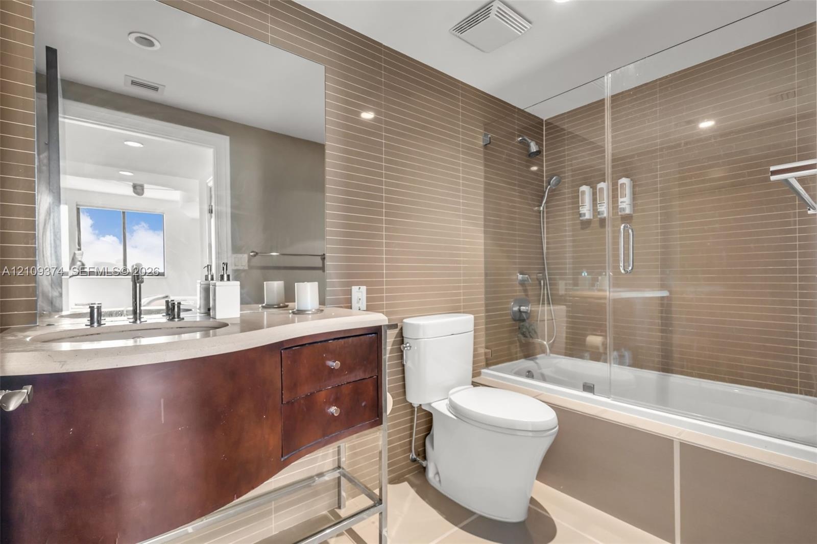 Bathroom featuring a curved vanity with stone countertop, horizontal tile wall accents, and a glass-enclosed shower and tub combination