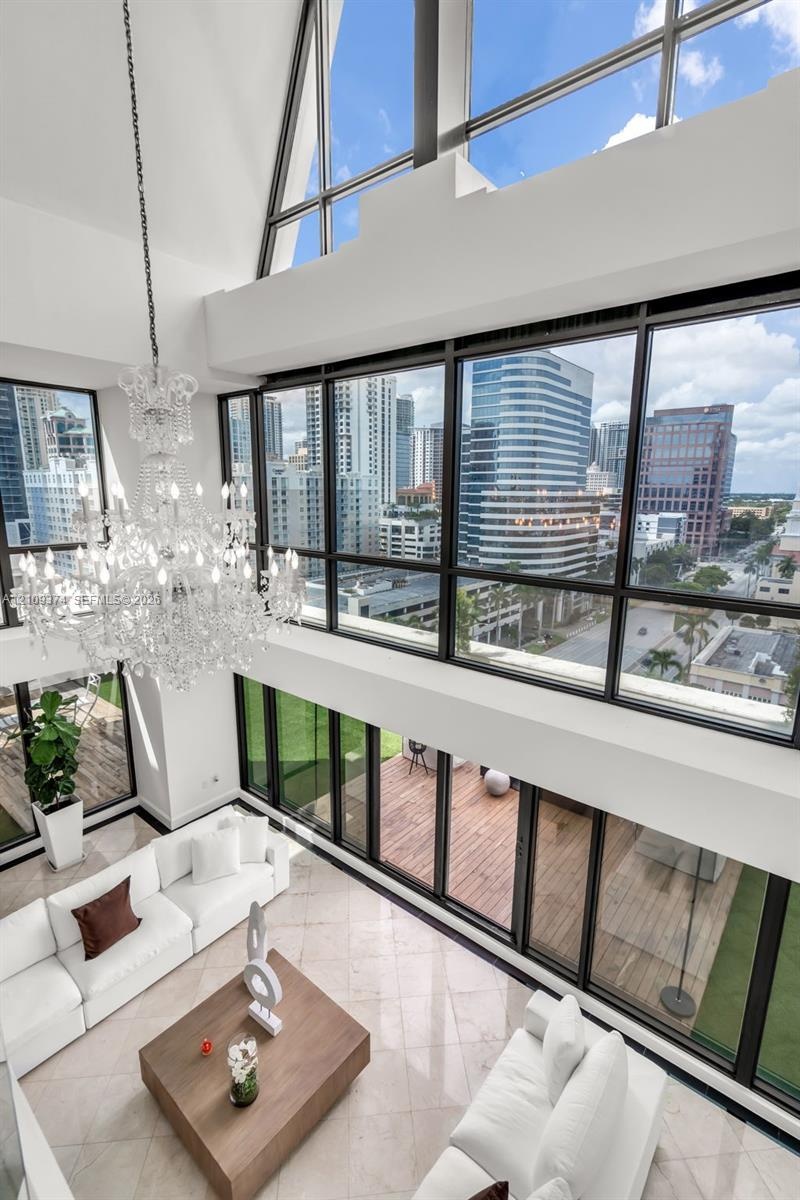 Double-height vaulted ceilings featuring floor-to-ceiling multi-story windows, polished stone flooring, intricate tiered crystal chandelier, and direc
