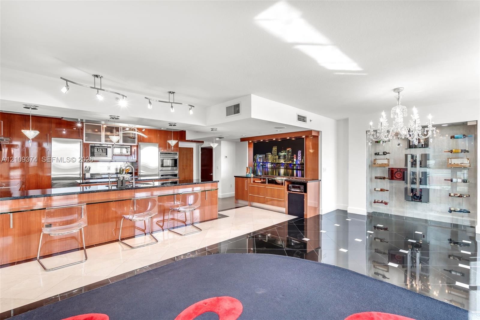 Modern kitchen featuring high-gloss cabinetry, dark stone countertops, built-in stainless steel appliances, a recessed wet bar, and a floor-to-ceiling