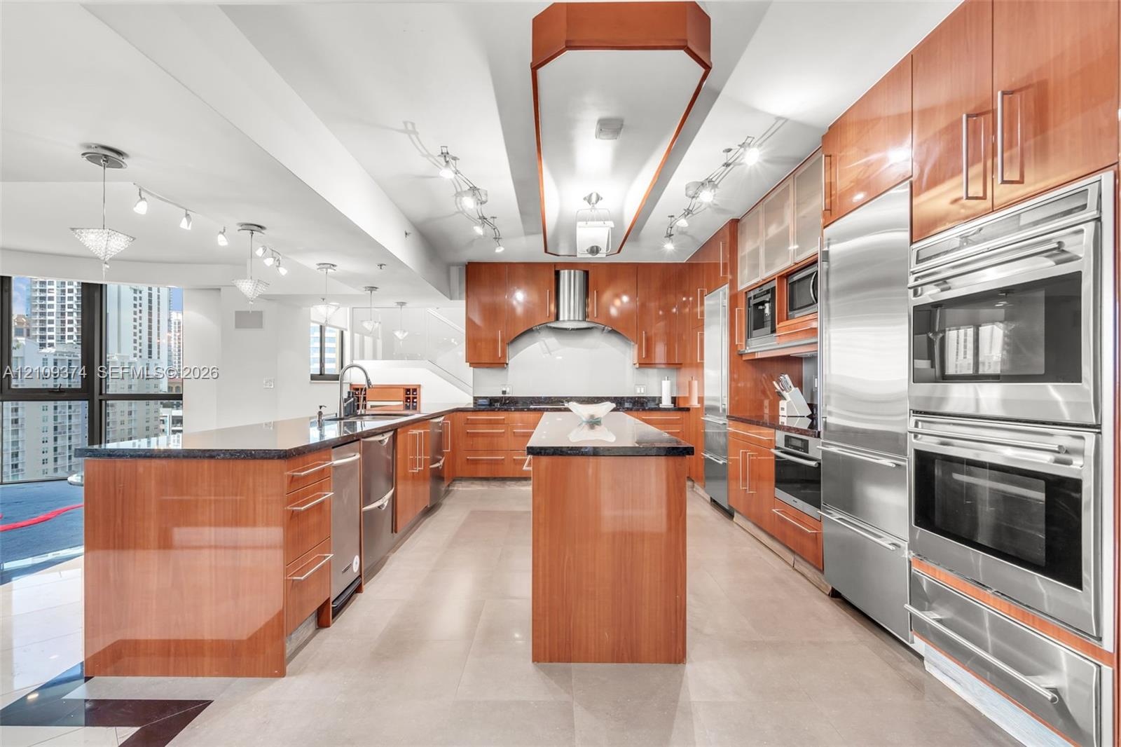 Contemporary kitchen featuring high-gloss cabinetry, stone countertops, double wall ovens, integrated stainless steel refrigeration, and a central isl