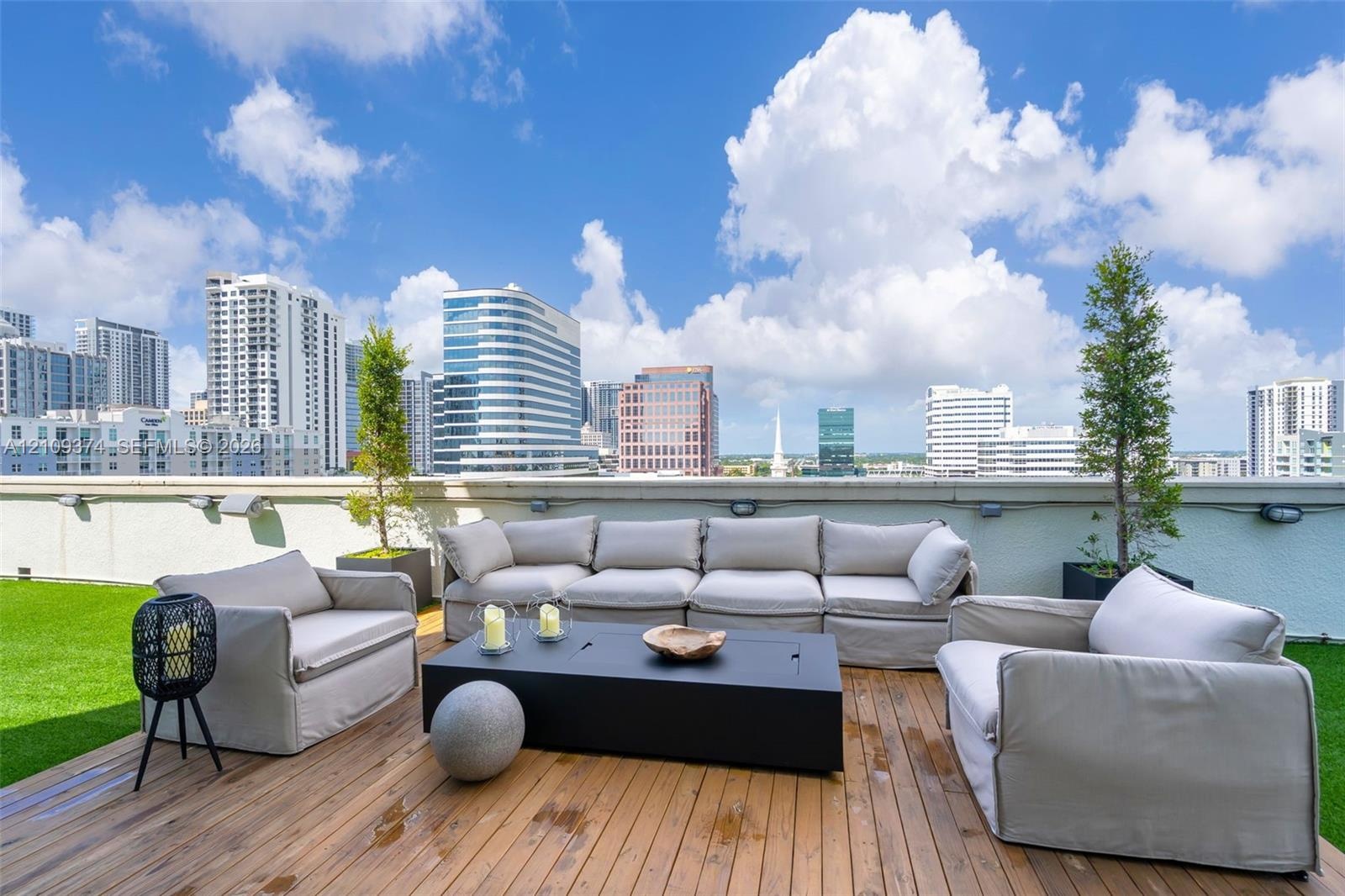 Expansive rooftop terrace featuring wood-plank decking, synthetic turf, integrated wall-mounted lighting, and panoramic urban skyline scenery
