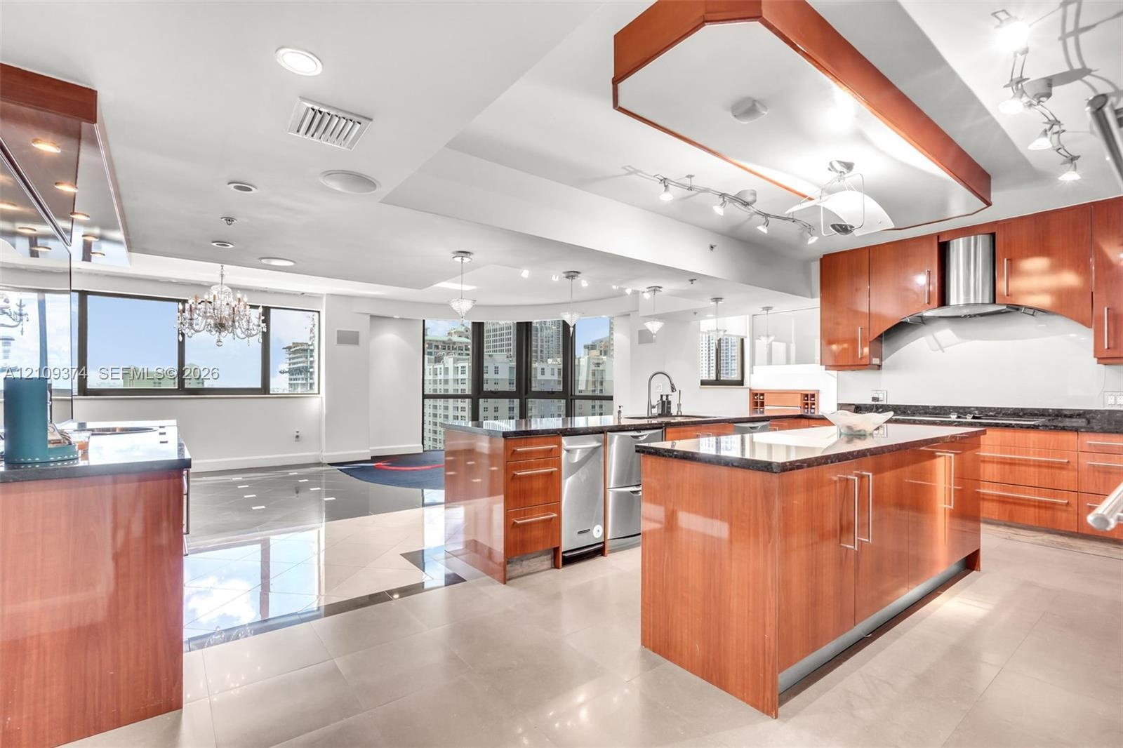 Kitchen featuring wood-finish cabinetry, stone-surface countertops, stainless steel appliances, tiered tray ceiling, and tile flooring