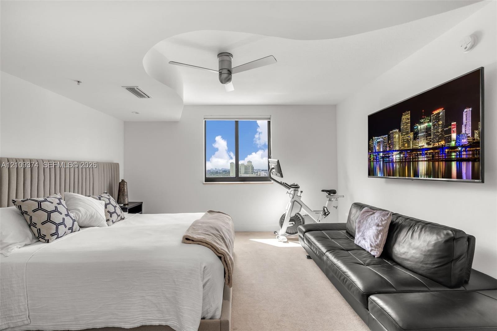 Custom tray ceiling featuring a curved architectural design, ceiling-mounted brushed-finish fan, wall-to-wall carpeting, and single-pane window