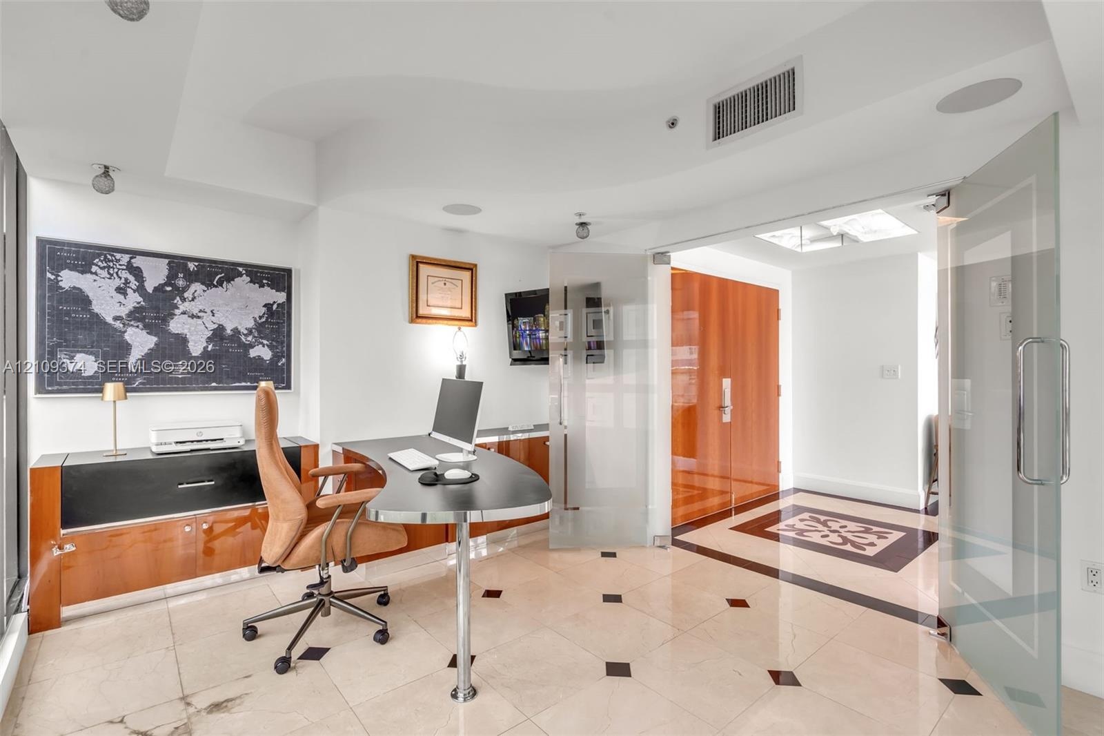 Light-filled room featuring large-format stone flooring with decorative inlay, custom wood-finish built-in cabinetry, frosted glass pivot entry doors,
