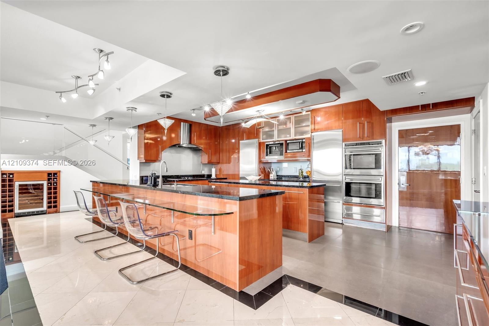 Gourmet kitchen featuring high-gloss wood cabinetry, dark stone countertops, integrated stainless steel appliances, a glass-top breakfast bar, and pol