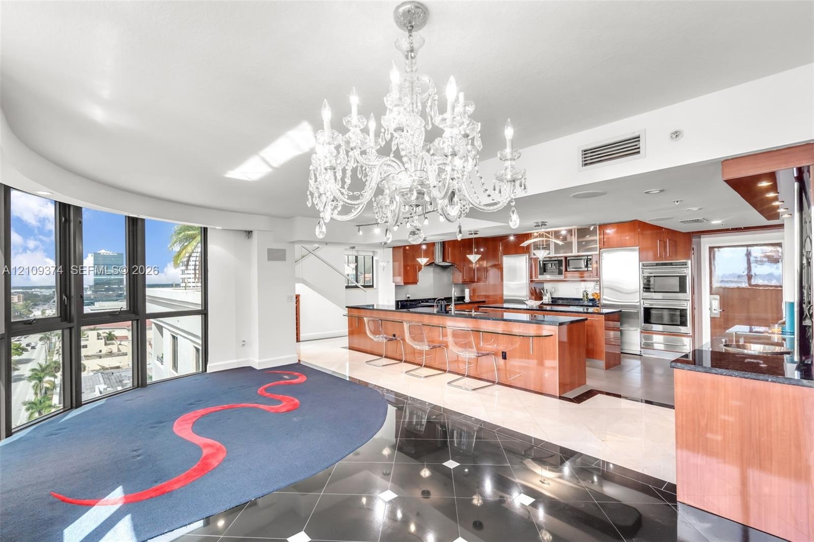 Kitchen featuring high-gloss wood cabinetry, dark stone countertops, built-in stainless steel appliances, a large center island, and an ornate crystal