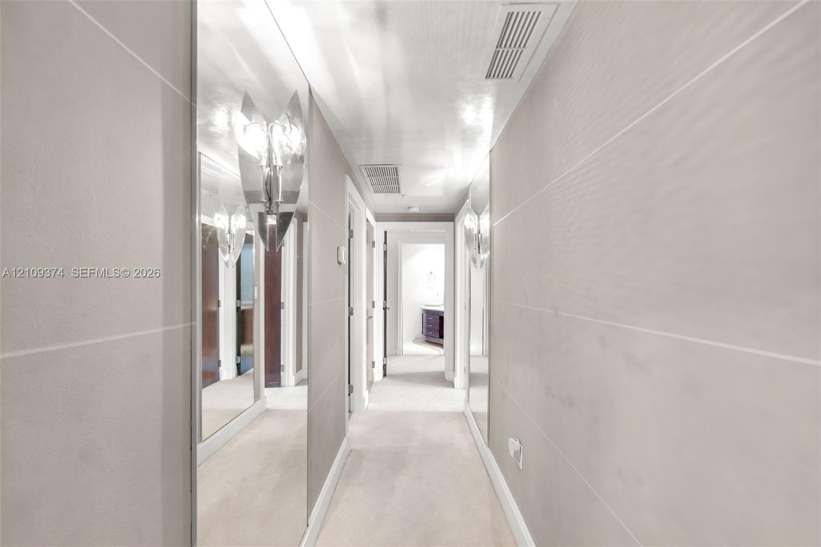 Hallway featuring large-format light-toned wall tile, floor-to-ceiling mirror panels, and dual metallic wall-mounted sconces