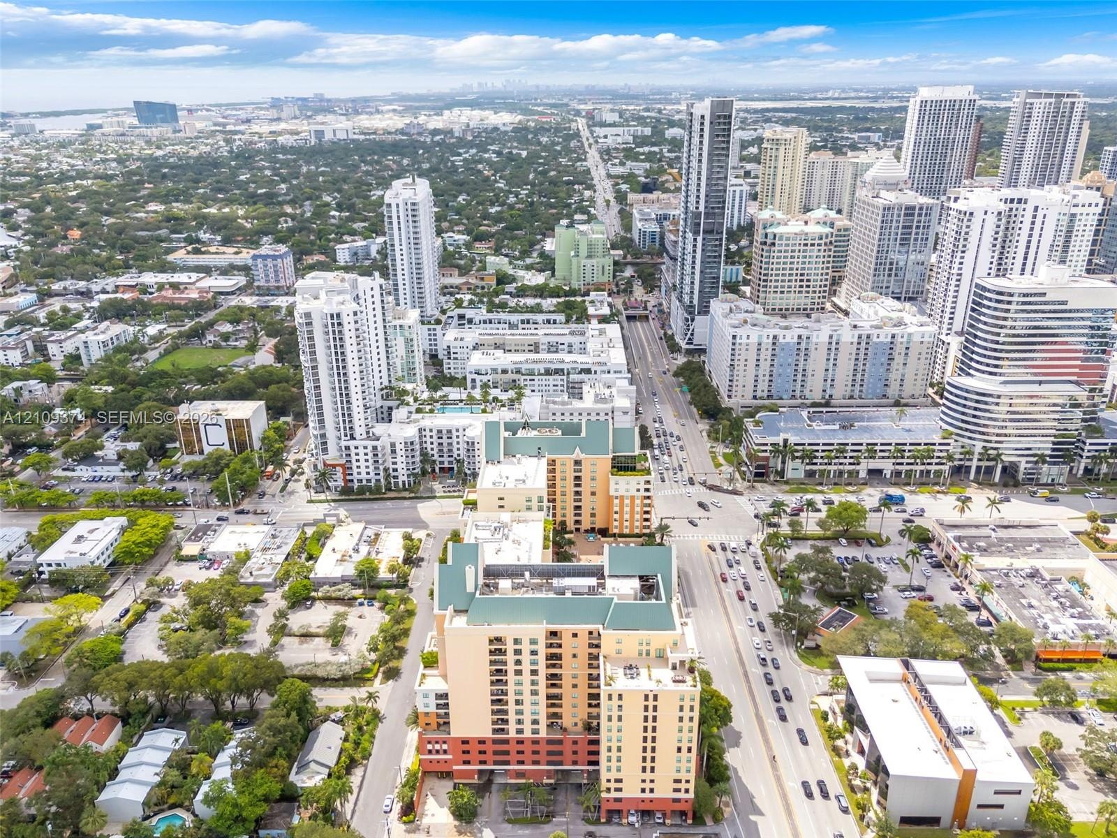 Aerial perspective of a multi-story urban complex featuring a prominent peaked roofline, stucco-finish facade, ground-level parking access, and extens