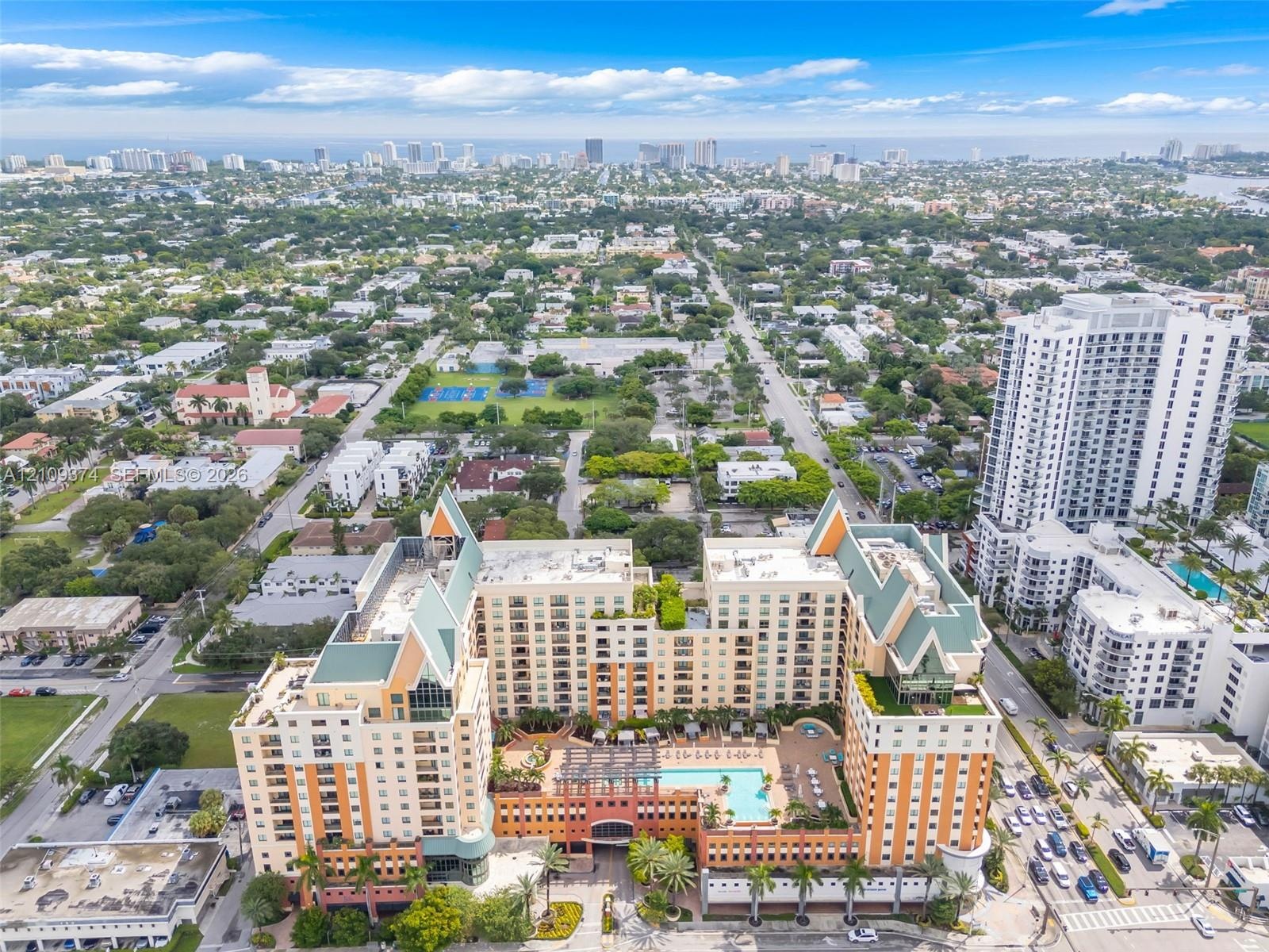Aerial perspective of a multi-story residential complex featuring a central outdoor swimming pool, terracotta-toned facade, decorative pitched roofing