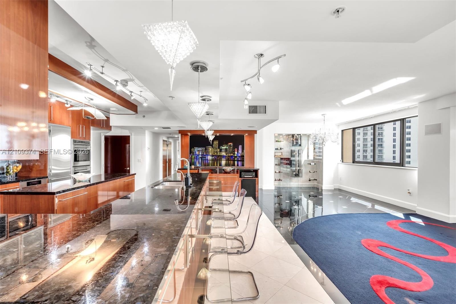 Contemporary kitchen featuring high-gloss wood-finish cabinetry, expansive stone countertops, integrated stainless steel appliances, a tiered island w
