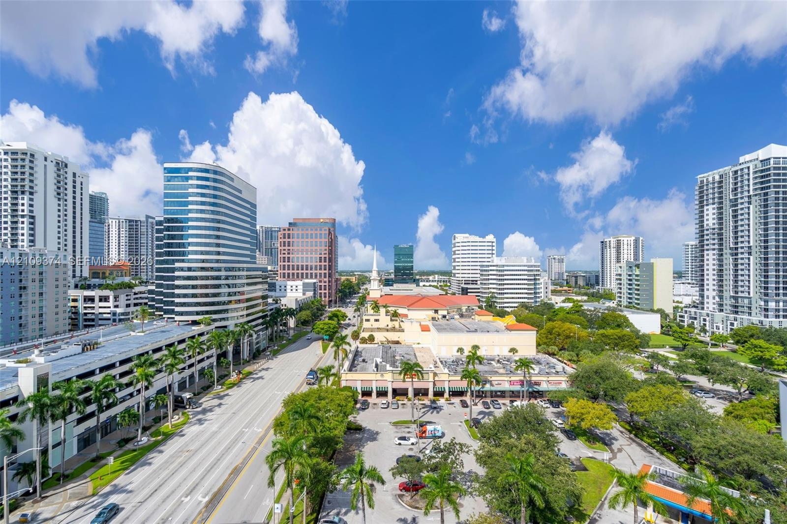 Aerial perspective of the urban landscape featuring high-rise architecture, prominent city thoroughfares, and lush palm tree landscaping