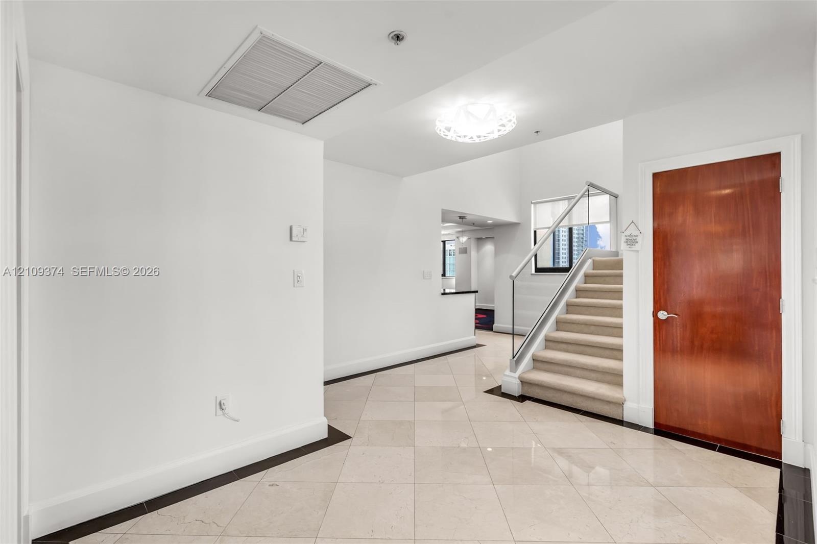 Entryway featuring large-format diagonal tile flooring, a solid wood-finish entry door, a staircase with a glass panel railing, and a decorative circu