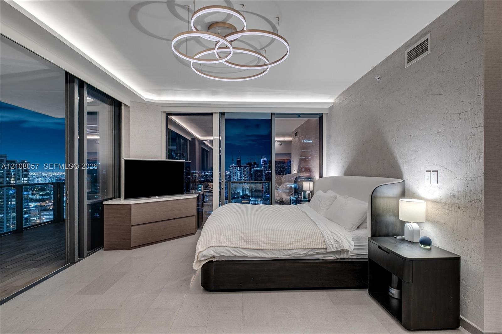 Floor-to-ceiling sliding glass walls, custom circular multi-tier light fixture, textured stone accent wall, recessed cove lighting, and stone flooring