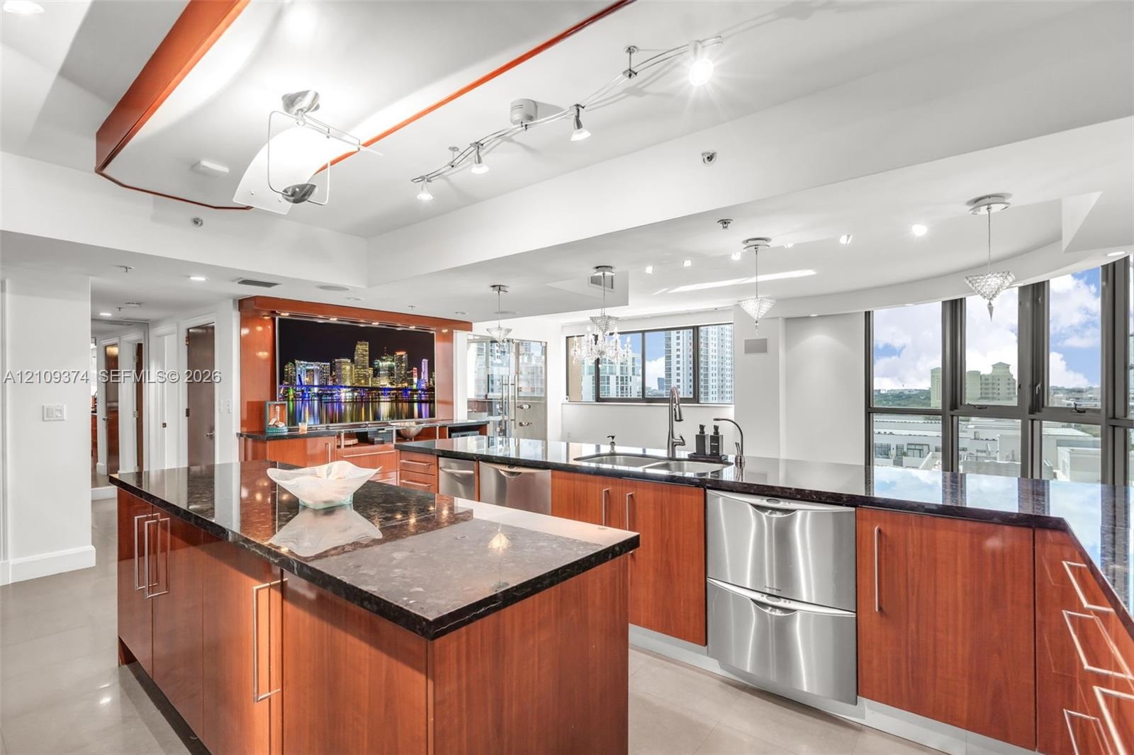 Kitchen featuring wood-veneer cabinetry, stone countertops, stainless steel appliances, tiered tray ceiling with recessed lighting, and floor-to-ceili