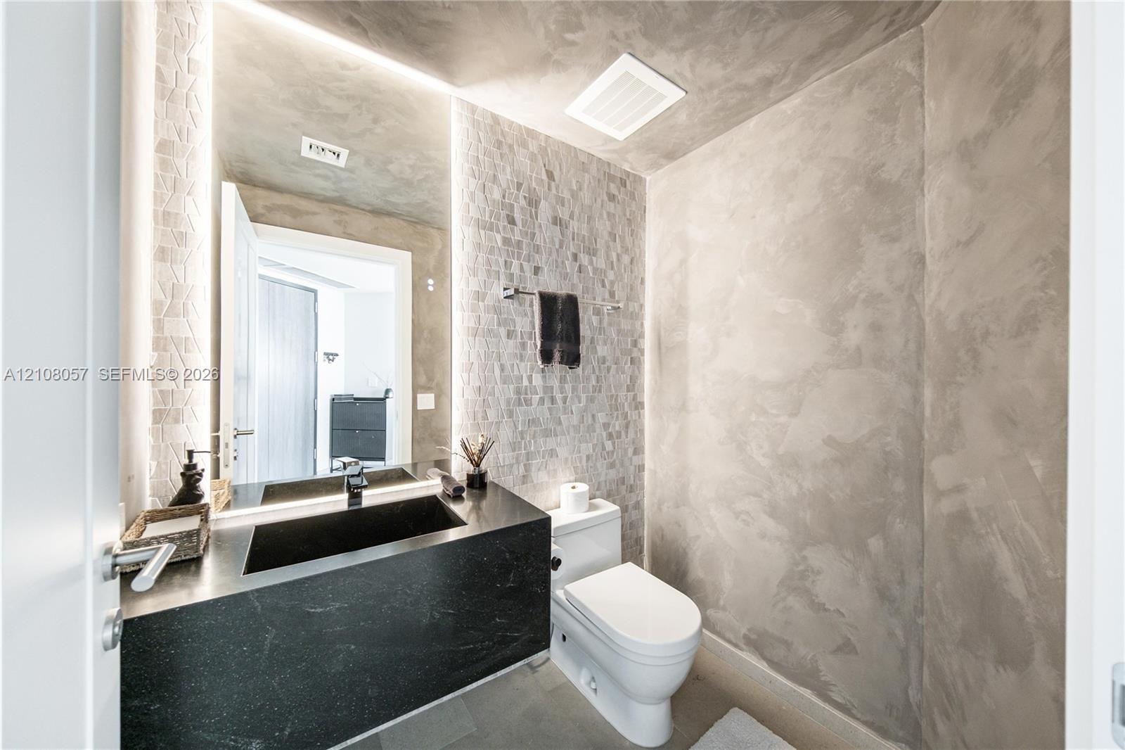Bathroom featuring textured wall finishes, a floating black countertop with an integrated basin, vertical recessed LED lighting, and mosaic-tiled acce