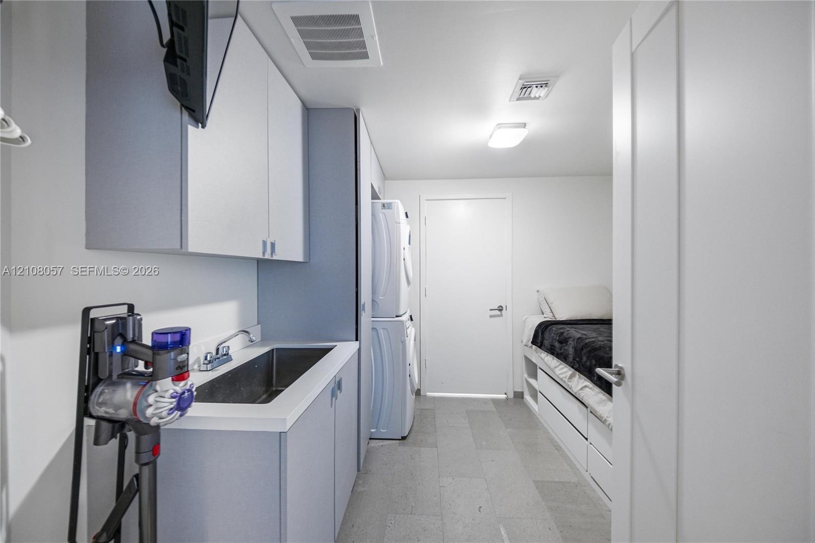Laundry area featuring built-in cabinetry, an integrated stainless steel basin with a dual-handle faucet, stacked laundry appliances, and tile floorin