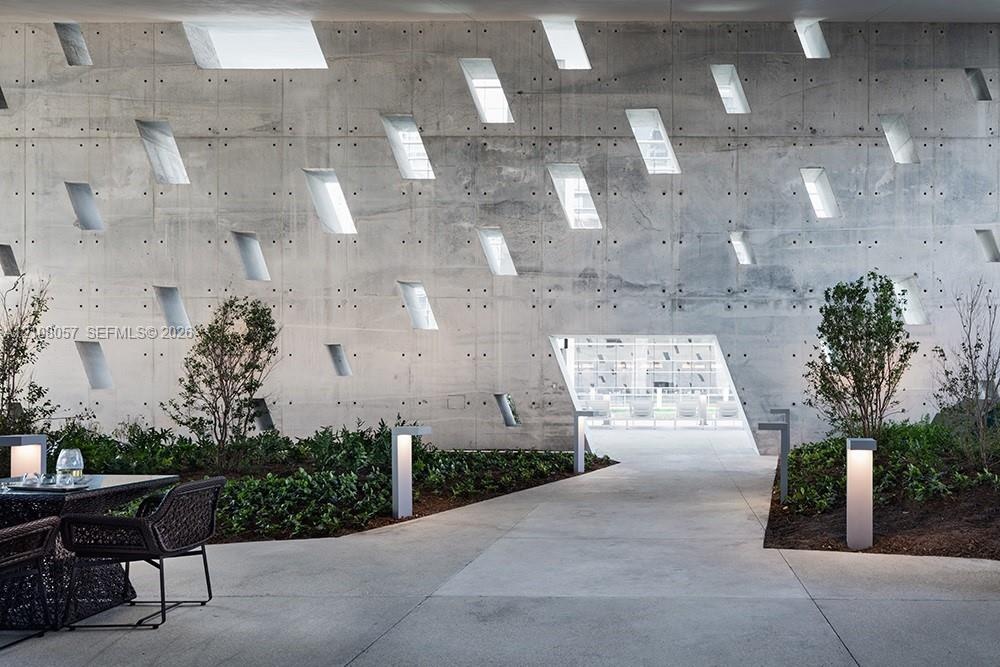 Architectural concrete wall featuring a geometric pattern of recessed window openings, cast-in-place construction, integrated landscape lighting, and 