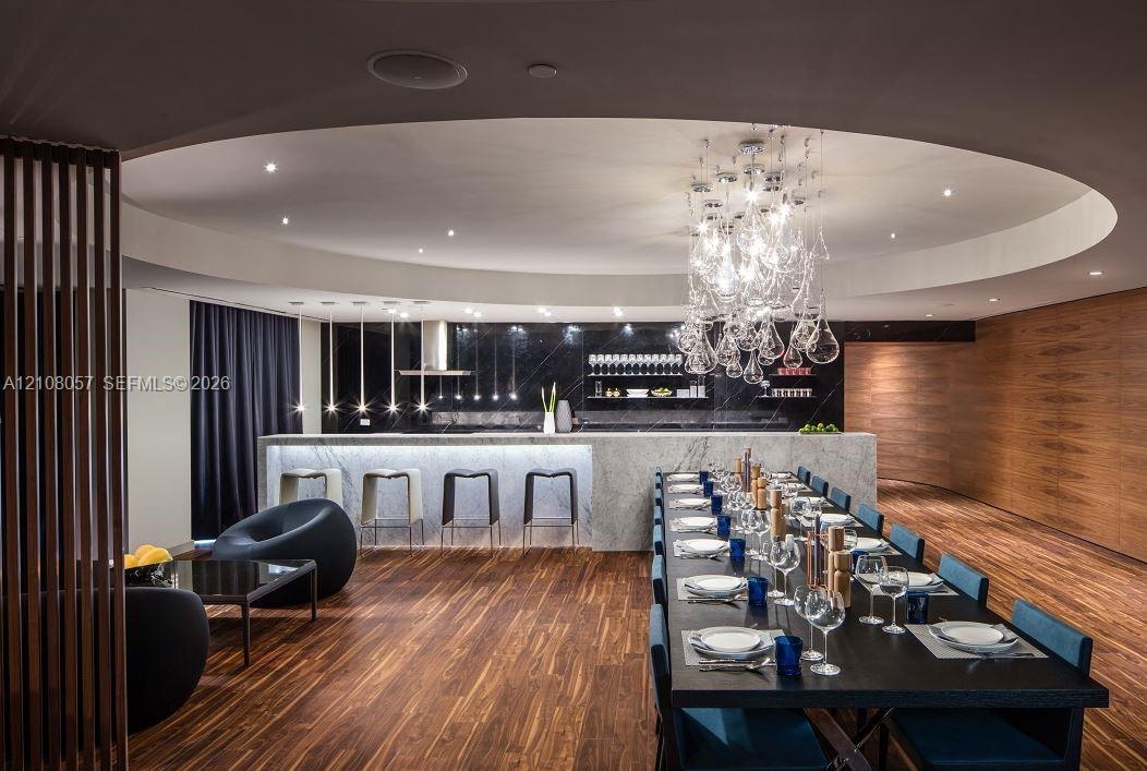 Circular recessed ceiling detail with a sculptural glass chandelier, wood-finish flooring, full-height wood-paneled walls, and a stone-topped island w