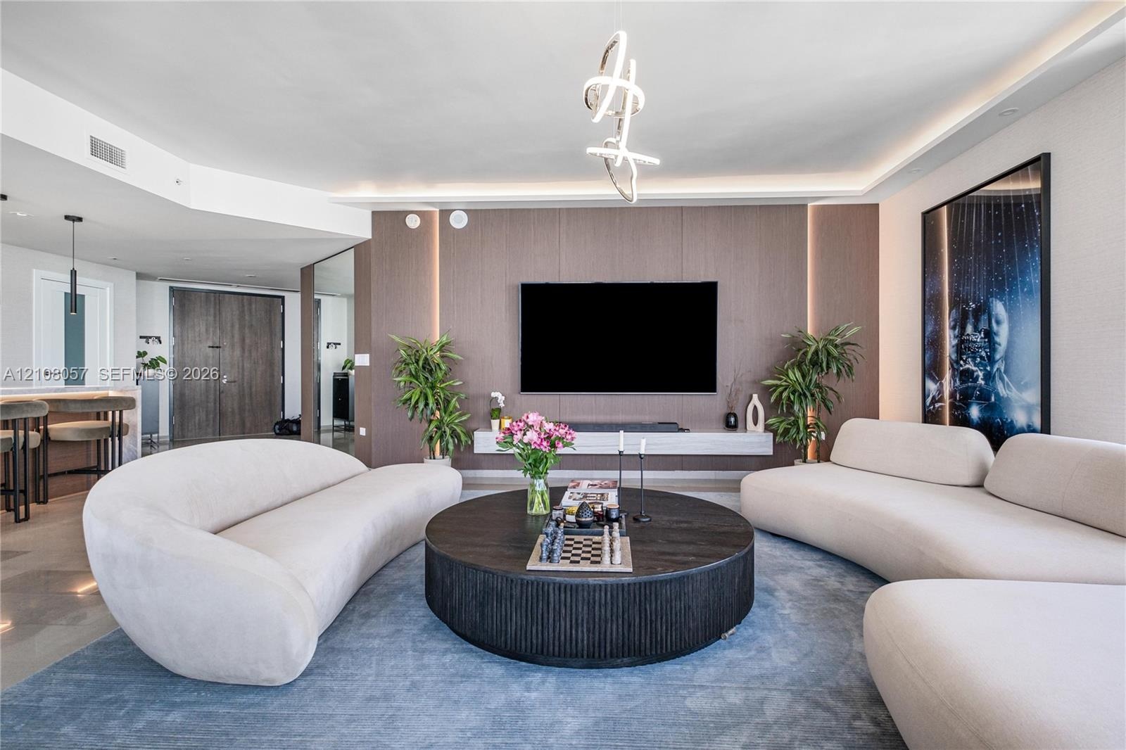 Living area featuring wood-paneled accent wall, floating media console, integrated vertical lighting, and sculptural chandelier