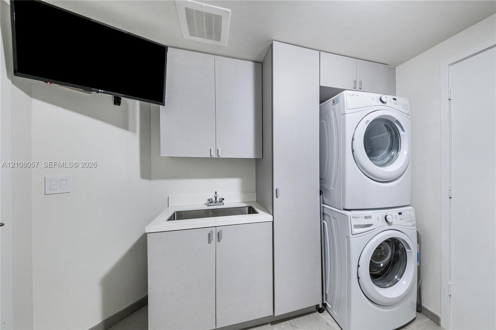 Laundry room featuring cabinetry with light-colored laminate finishes, a rectangular drop-in sink, and a vertical stacked laundry center
