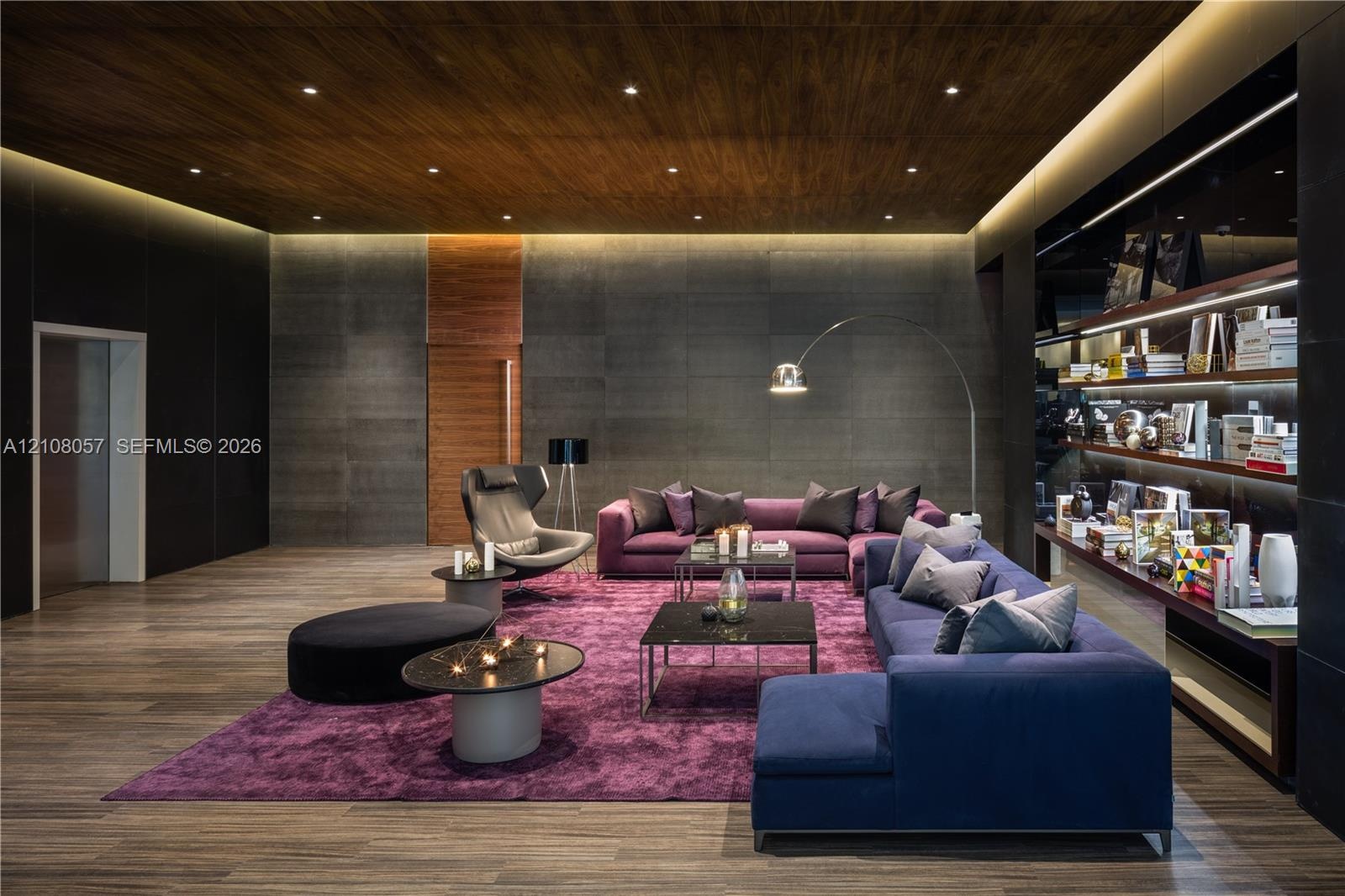 Wood-finish flooring, dark stone wall cladding, wood-paneled ceiling with recessed lighting, integrated cove lighting, and built-in wall shelving with