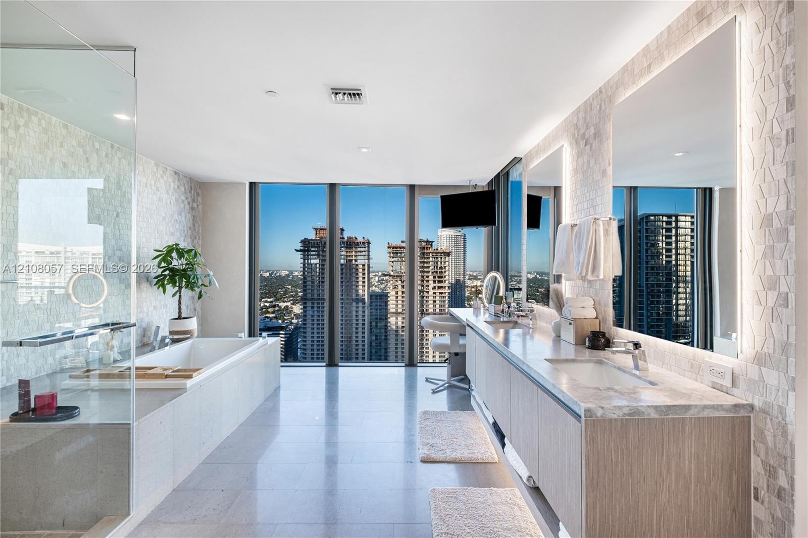 Floor-to-ceiling windows, dual-sink vanity with wood-finish cabinetry, stone countertop, glass-enclosed shower, and built-in soaking tub