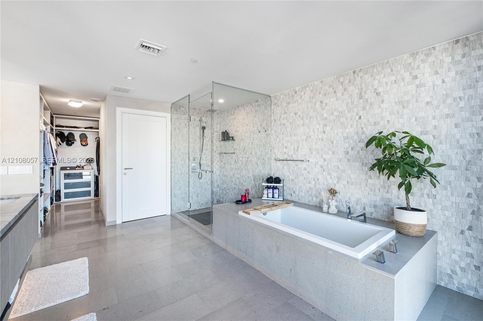 Bathroom featuring a deep-soaking drop-in tub with a stone-surround deck, a seamless glass-enclosed shower, stone mosaic wall tiling, large-format flo