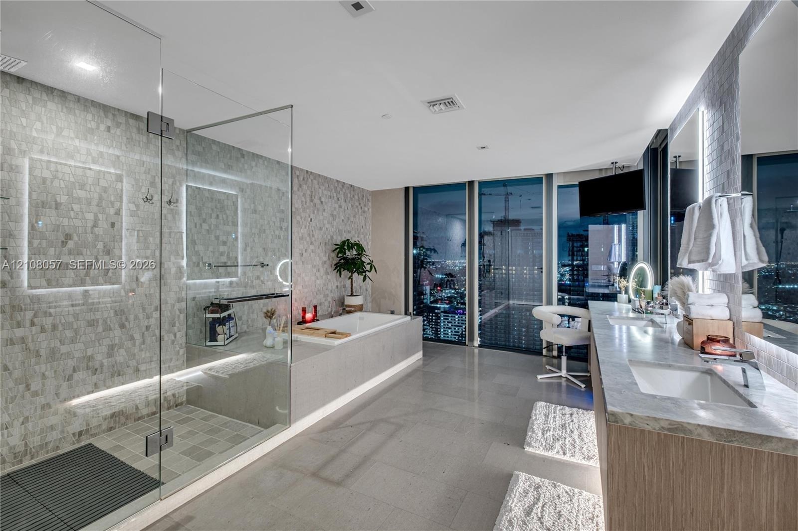 Bathroom featuring floor-to-ceiling windows, a glass-enclosed walk-in shower with stone tile wall, a soaking tub with stone surround, and a dual-sink 