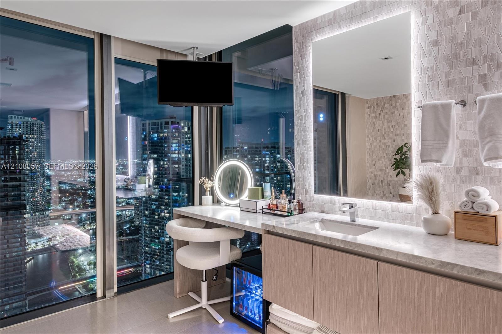 Floor-to-ceiling windows, custom vanity with integrated seating, stone countertop, undermount sink, and illuminated wall-mounted mirror