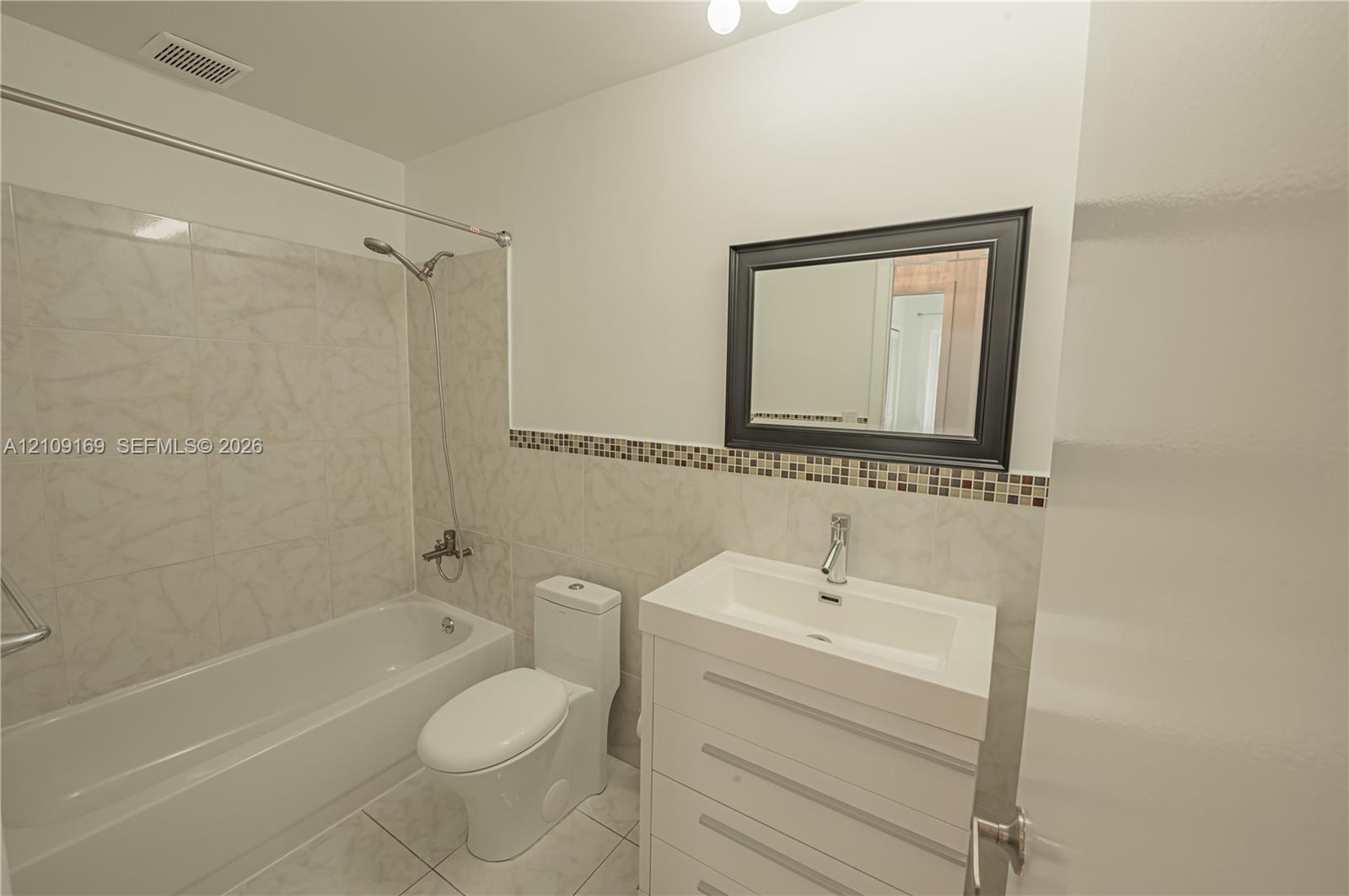 Bathroom featuring a white vanity cabinet with a rectangular integrated sink, neutral stone-finish tile wainscoting with a glass mosaic accent border,