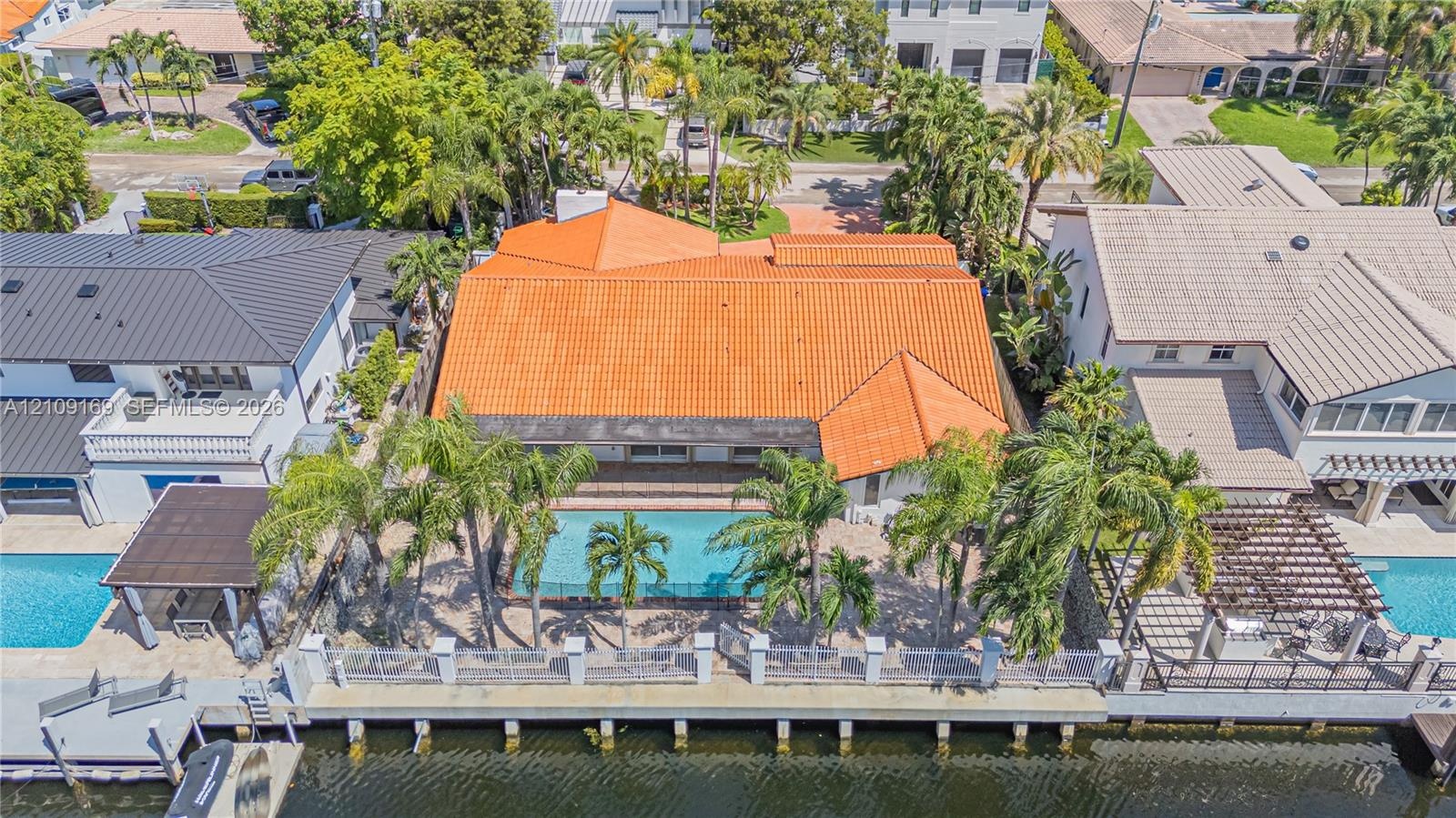Waterfront residence featuring a tiled roof, private swimming pool, concrete bulkhead, and mature palm trees
