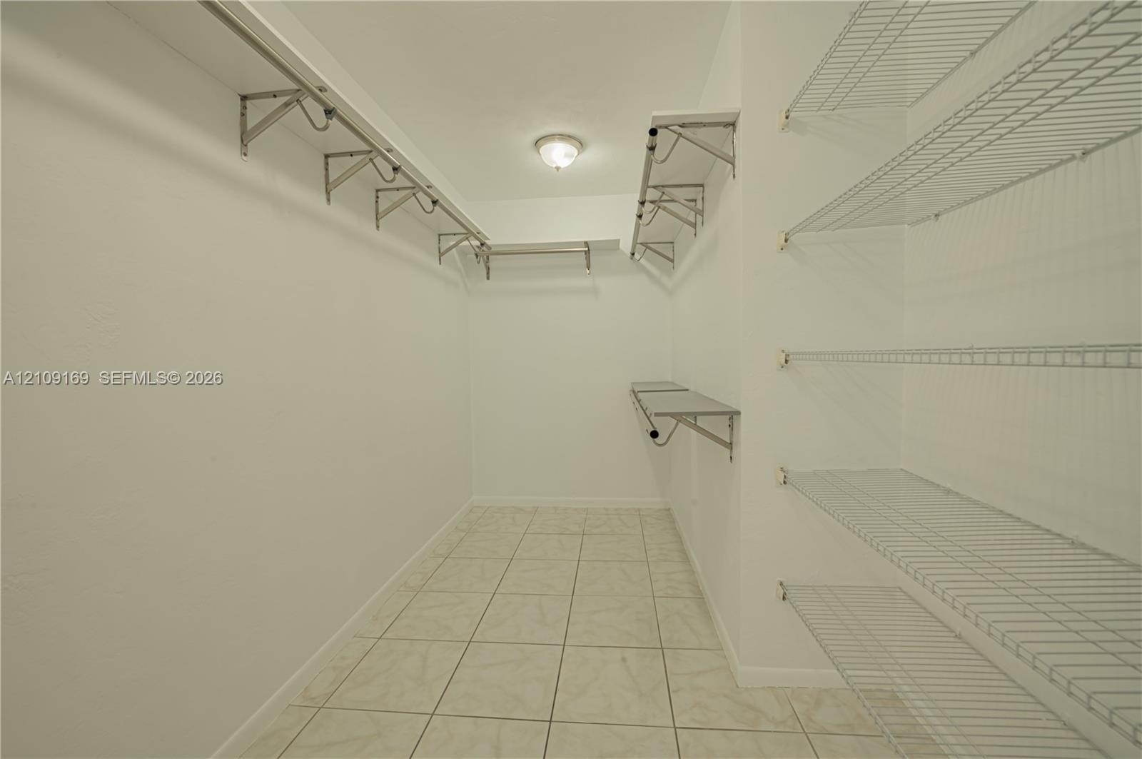 Walk-in storage space featuring ceramic tile flooring, multi-level wire shelving, and a centralized ceiling-mounted light fixture