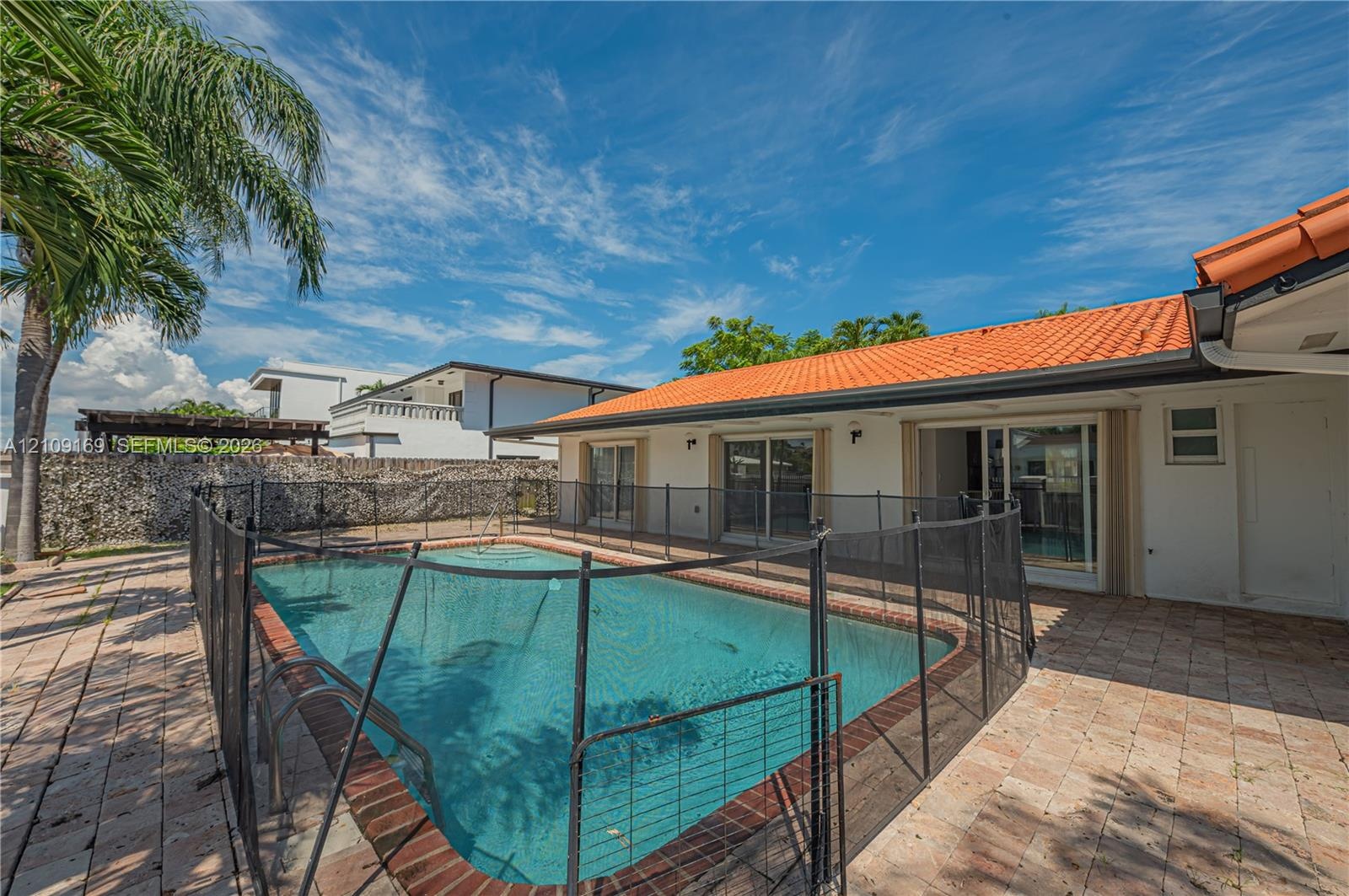 Exterior space featuring an in-ground swimming pool, terracotta-colored roof tiles, light-toned masonry walls, and brick-paver hardscaping