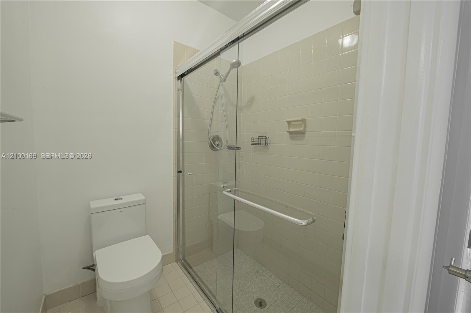 Walk-in shower featuring a sliding glass enclosure, ceramic tile surround, integrated shower bench, and a handheld shower fixture, paired with a dual-