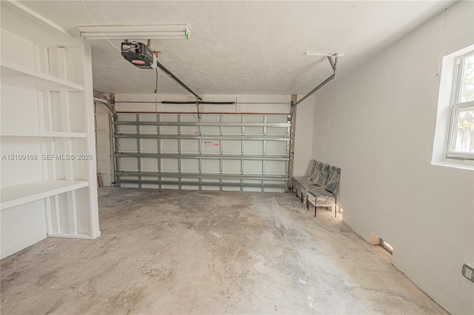 Multi-car garage featuring concrete flooring, built-in wall shelving, a mechanical door system, and a single-pane window