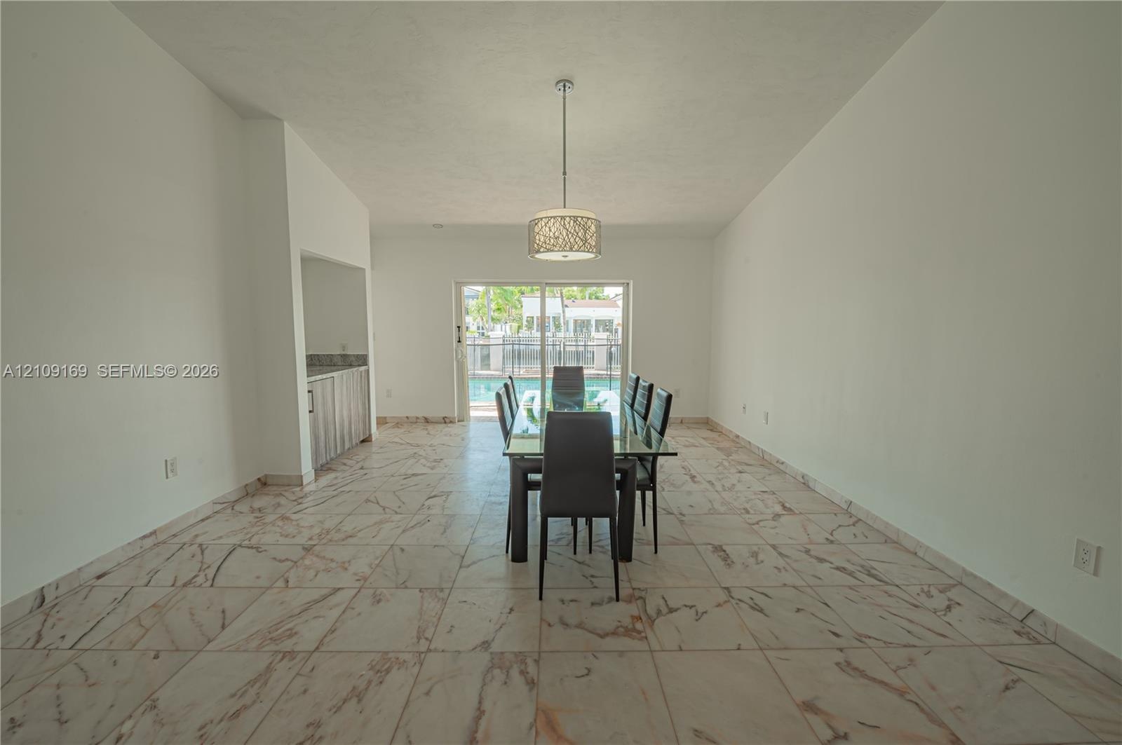 Vaulted ceilings, large-format tile flooring with veined detail, built-in wet bar, cylindrical pendant light fixture, and sliding glass doors opening 