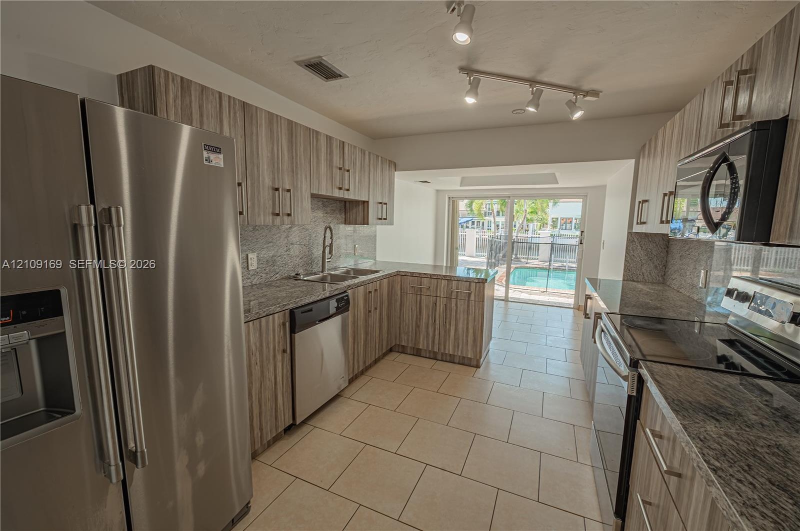 Kitchen featuring wood-finish cabinetry, stone-surface countertops, stainless steel appliances, ceramic tile flooring, and adjustable track lighting