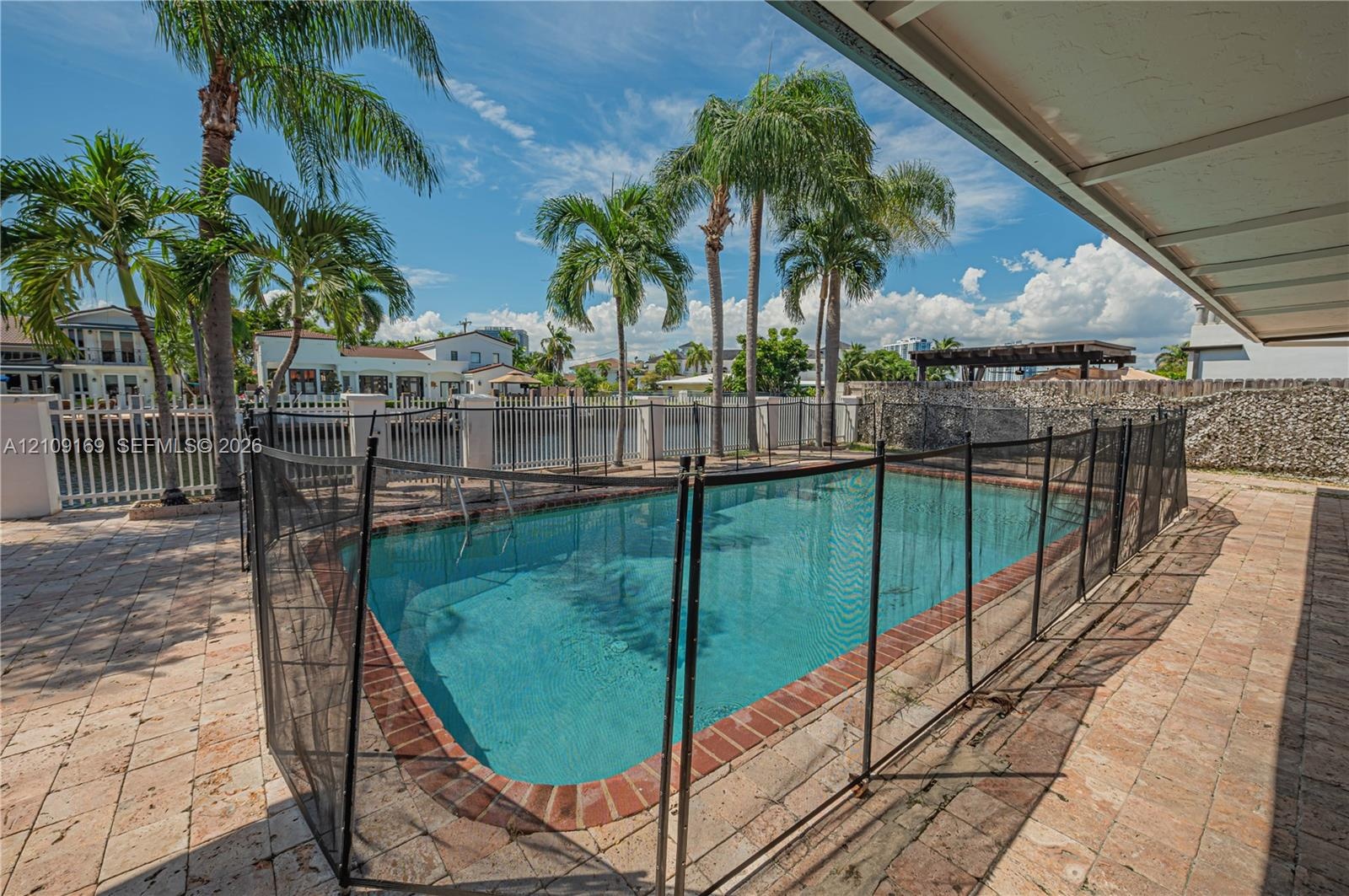 In-ground swimming pool with a brick surround, paver patio, stone perimeter wall, and mature palm trees