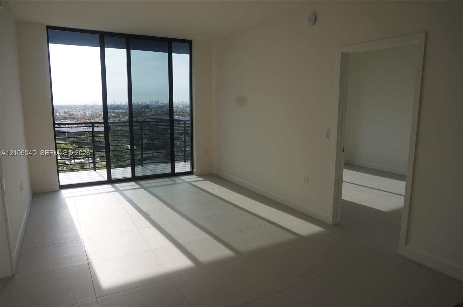 Floor-to-ceiling sliding glass doors, private balcony with metal railing, and neutral tile flooring