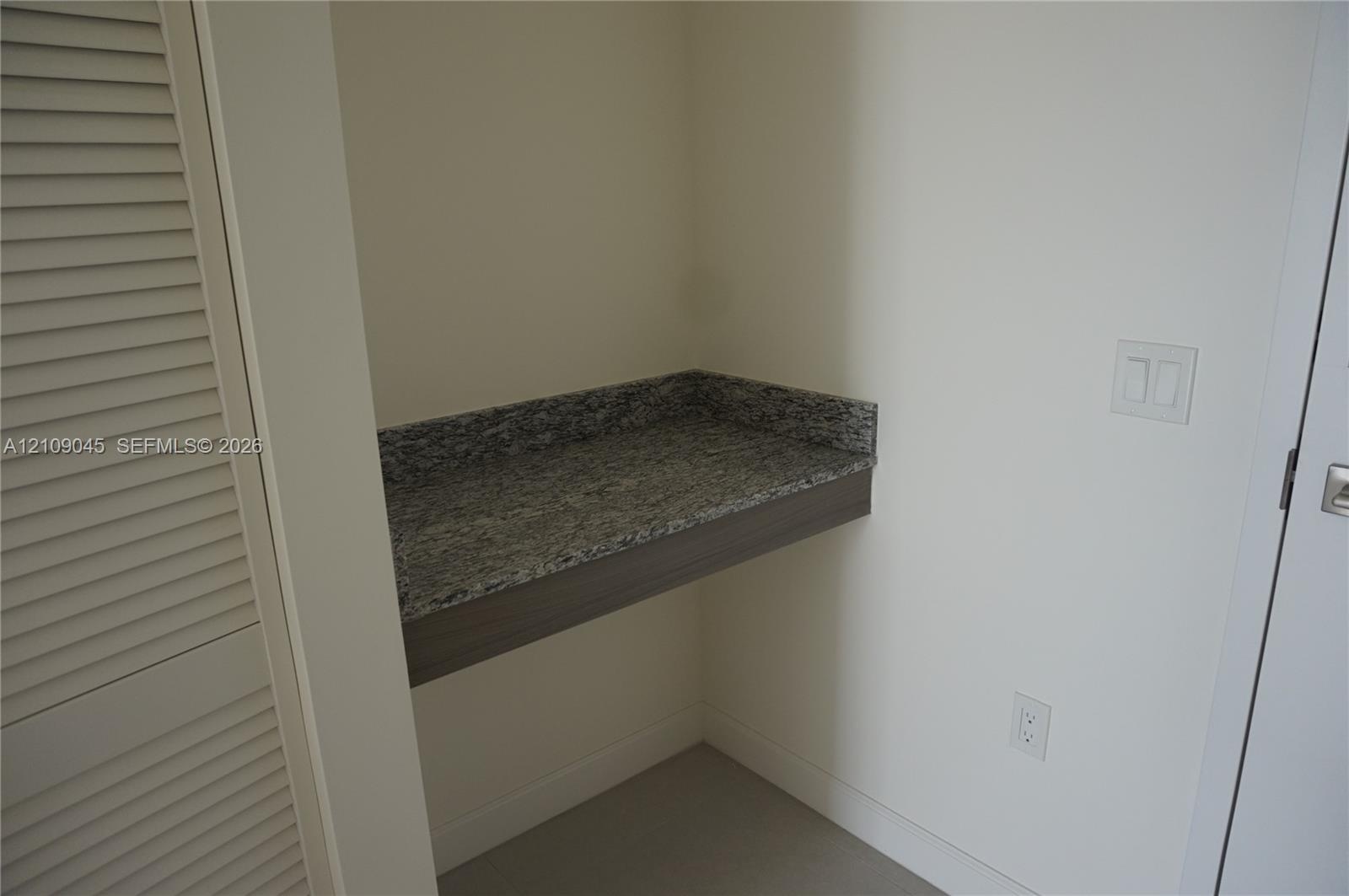 Built-in recessed workstation featuring a stone countertop, wood-finish apron, and louvered closet door