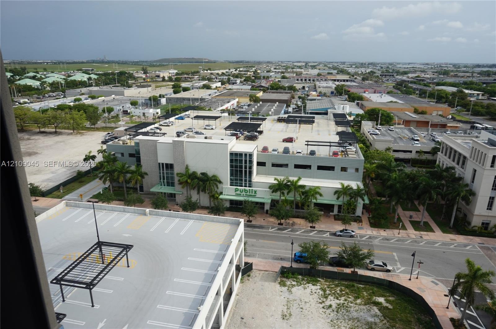Aerial perspective featuring a multi-level parking structure with shaded upper-level canopy units, mature palm trees, and paved street access within a