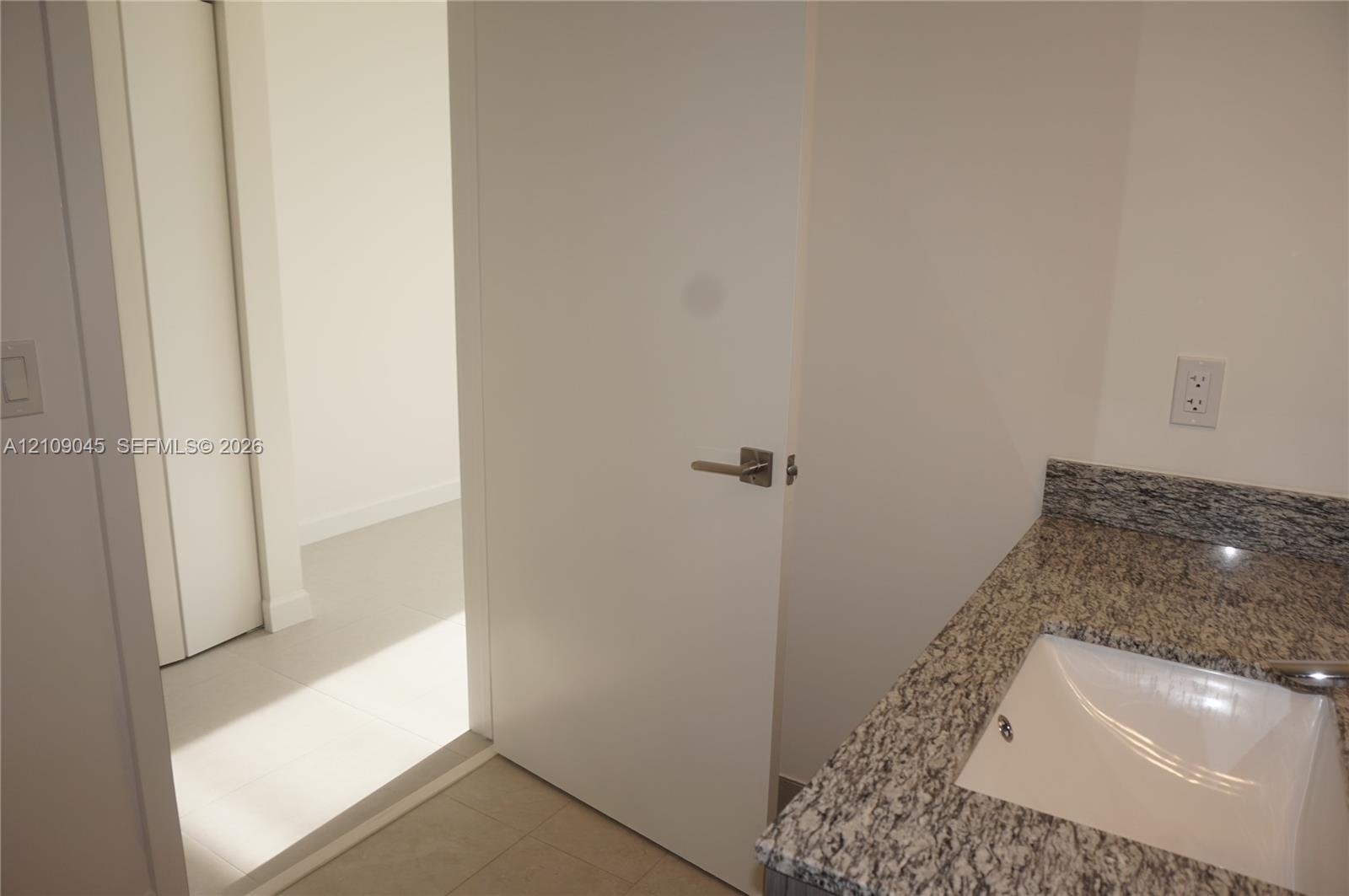 Stone-finish countertop featuring an integrated rectangular sink and modern metal hardware, complemented by neutral tile flooring and a solid-core doo