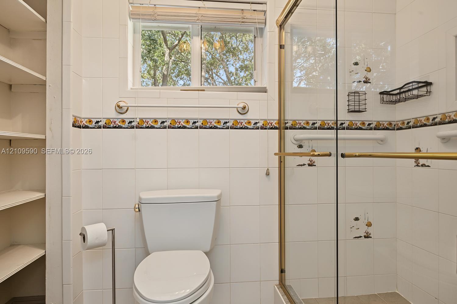 Bathroom featuring white wall tiling with decorative accent trim, glass-enclosed shower with gold-tone hardware, built-in recessed shelving, and a dou