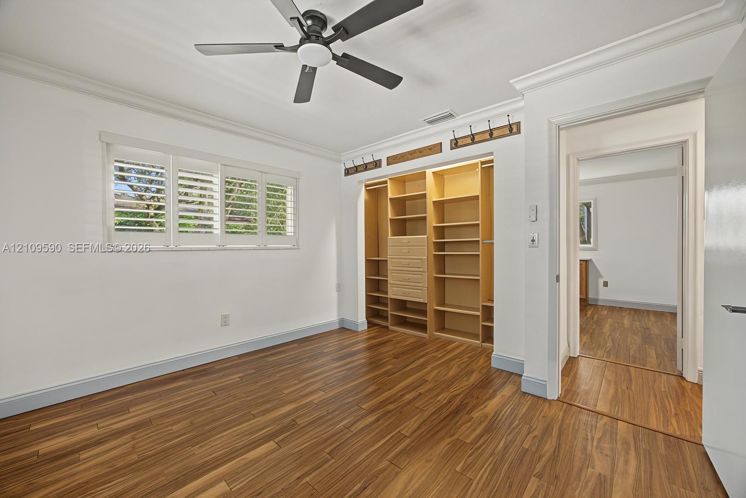 Bedroom 4 - Wood-finish flooring, custom built-in cabinetry, adjustable interior window shutters, ceiling fan, and crown molding