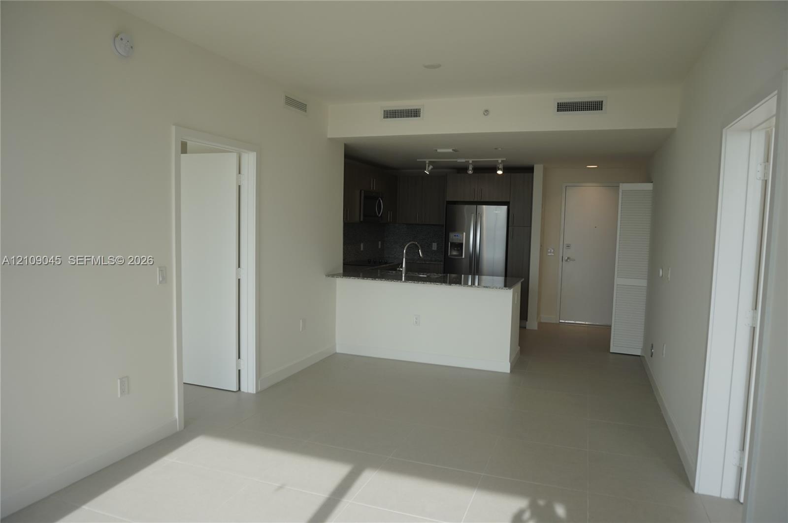 Open-concept kitchen featuring dark flat-panel cabinetry, stone countertops, stainless steel appliances, a gooseneck faucet, and large-format tile flo