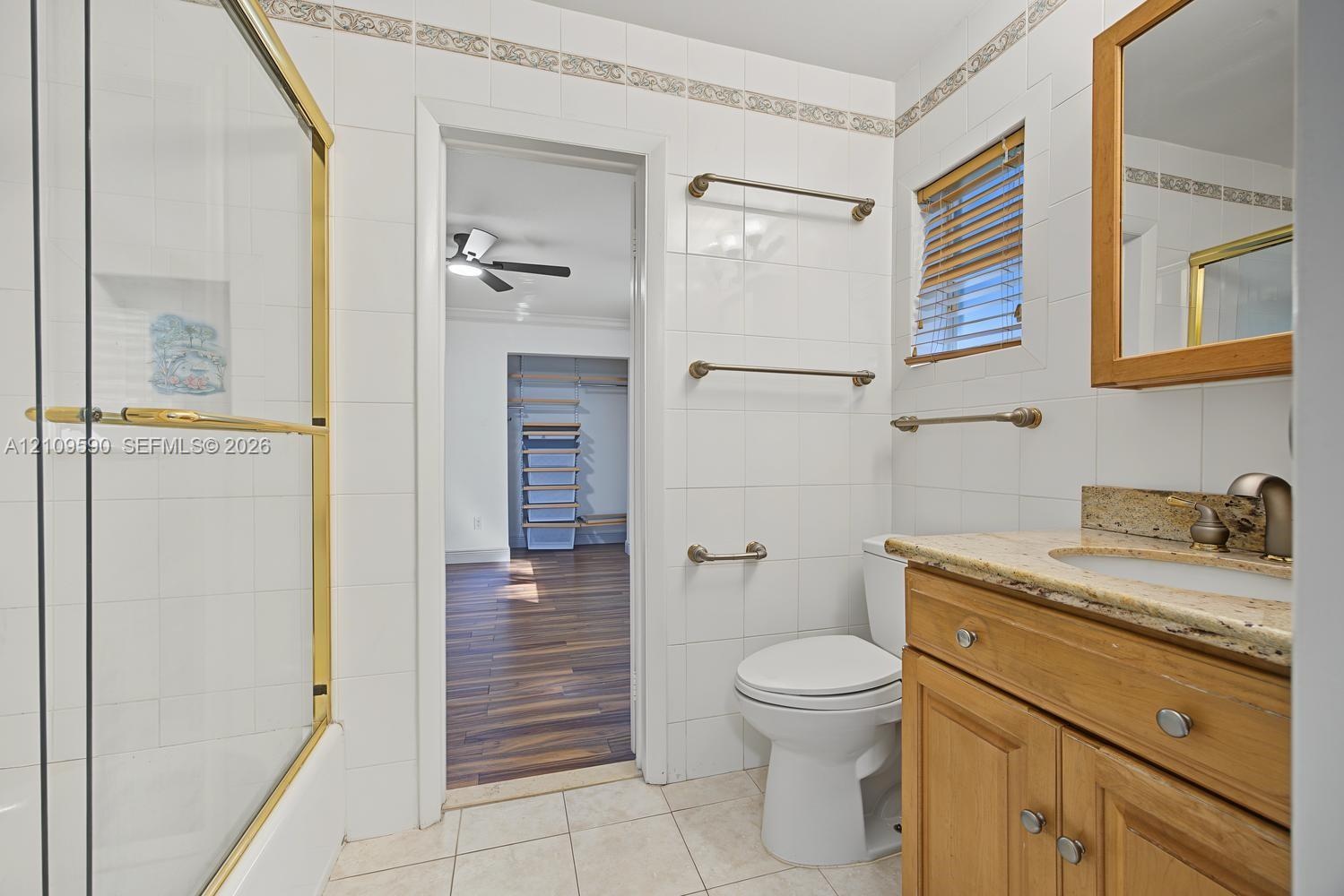 Bathroom featuring a wood vanity with a stone countertop, a shower with brass-finish framing, tiled walls, and ceramic tile flooring
