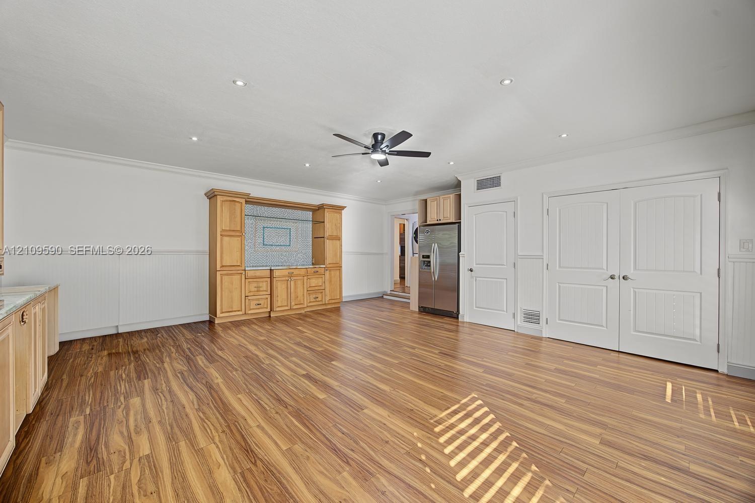 Open floor plan featuring wood-finish flooring, built-in wooden cabinetry with tiled backsplash, recessed ceiling lighting, a central ceiling fan, and