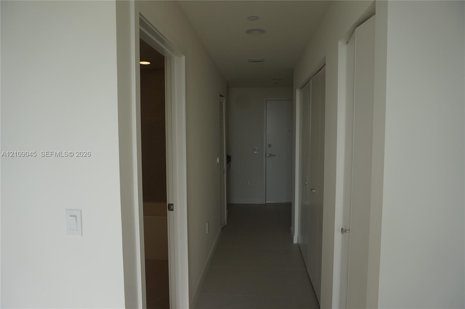 Interior hallway featuring neutral wall paint, recessed lighting, tile flooring, and multiple bifold closet doors